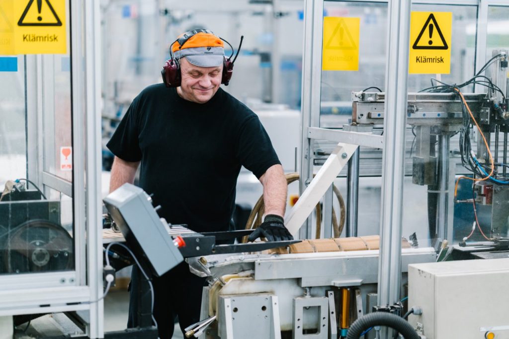 Fredmanin tehtaalla hymyilevä tehtaan työntekijä valmistaa elintarvikepakkauksia linjastolla.